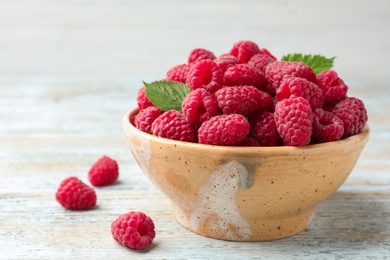 Photo of Bowl of delicious fresh ripe raspberries with leaves on wooden table, space for text