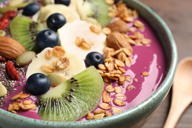 Delicious acai smoothie with granola and fruits in bowl on table, closeup