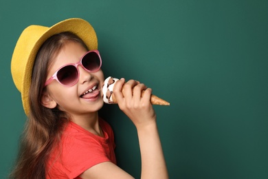 Cute little girl with delicious ice cream against color background, space for text