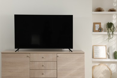 Stylish wide TV set on wooden cabinet in room