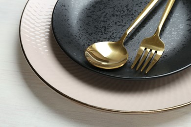 Stylish ceramic plates, fork and spoon on white wooden table, closeup