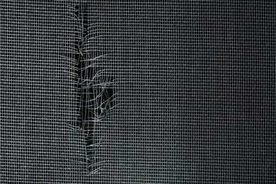 Torn window screen against black background, closeup