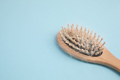 Wooden brush with lost hair on light blue background, closeup. Space for text