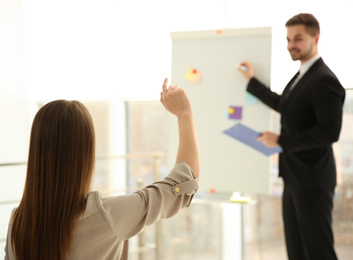 Young woman raising hand to ask question at business training indoors