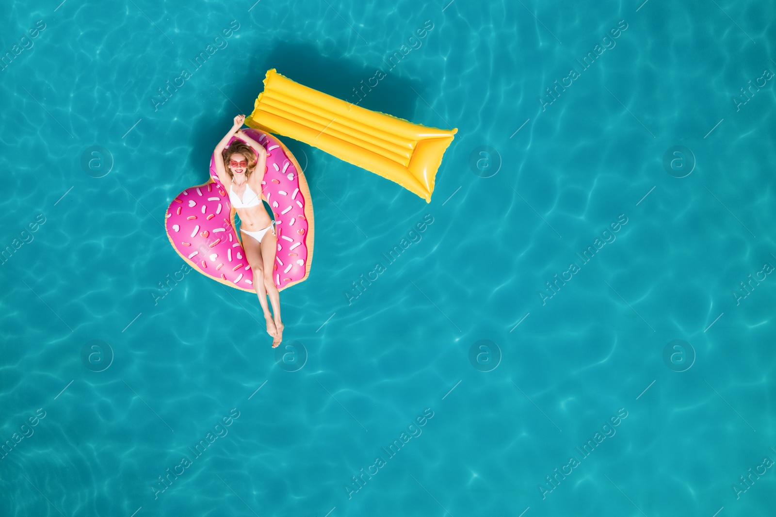 Image of Happy woman with inflatable mattress and ring in swimming pool, top view. Summer vacation