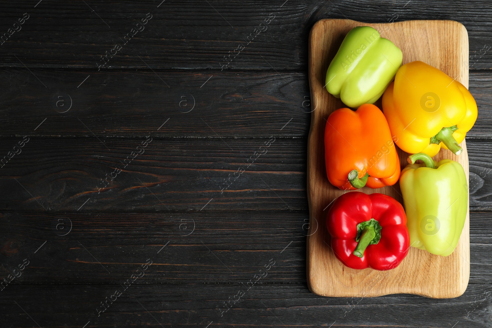 Photo of Board with ripe bell peppers on black wooden table, top view. Space for text