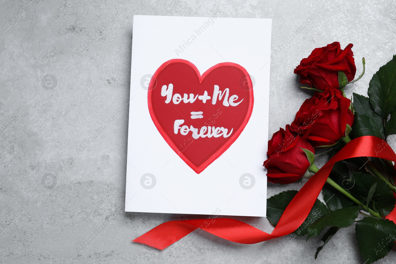Photo of Card with love message near red roses on grey table, flat lay