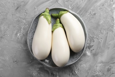 Fresh white eggplants in bowl on grey textured table, top view