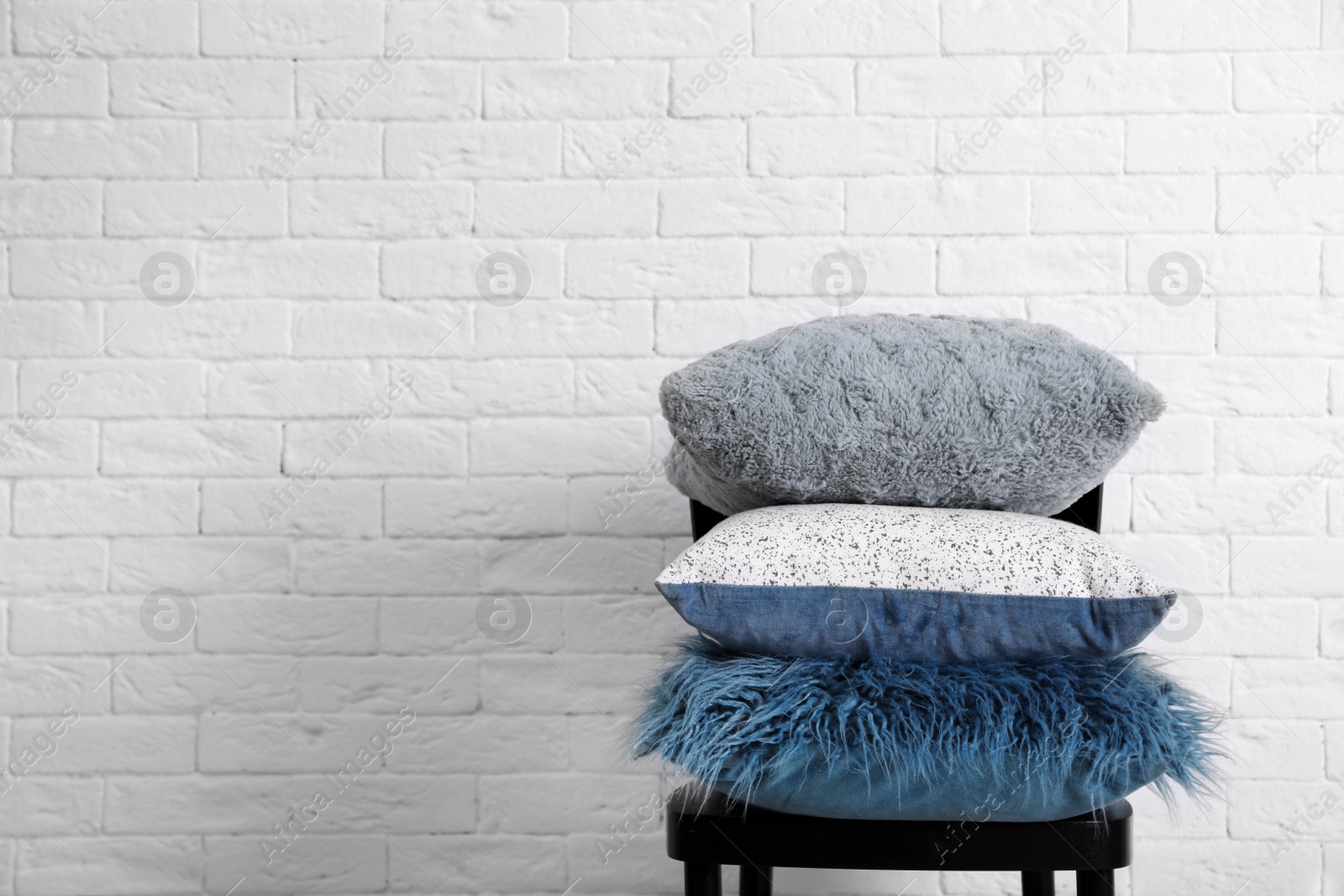 Photo of Many different pillows on chair near brick wall with space for text