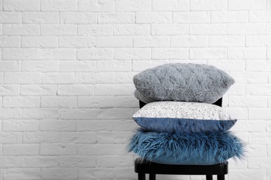 Photo of Many different pillows on chair near brick wall with space for text