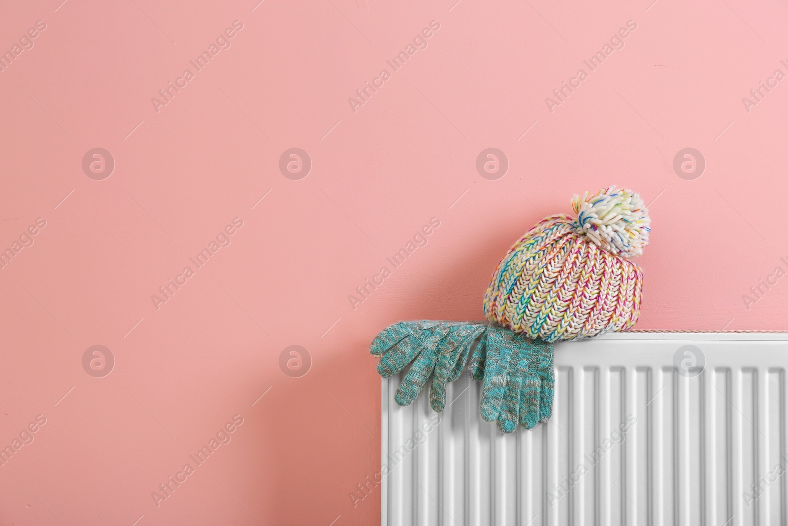 Photo of Heating radiator with knitted cap and gloves near color wall.Space for text