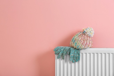 Photo of Heating radiator with knitted cap and gloves near color wall.Space for text
