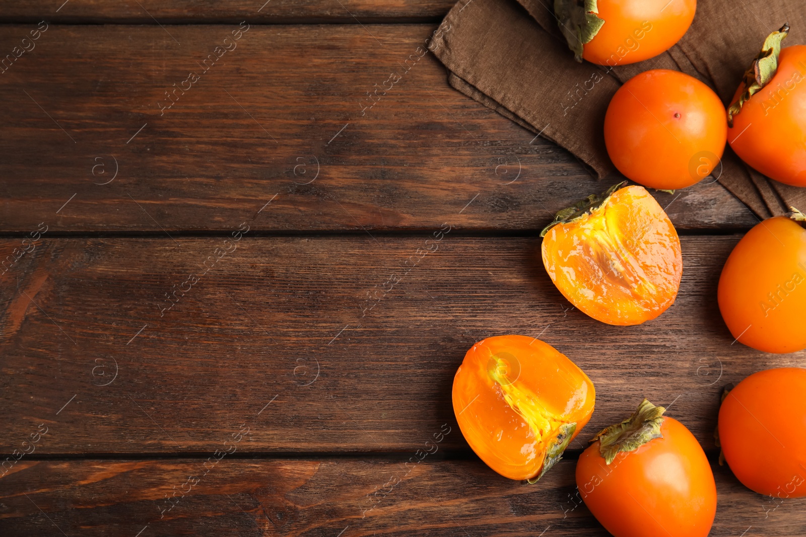 Photo of Delicious fresh persimmons on brown wooden table, flat lay. Space for text