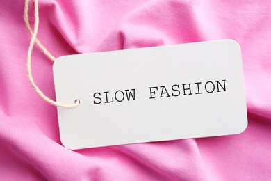 Image of Conscious consumption. Tag with words Slow Fashion on pink fabric, top view
