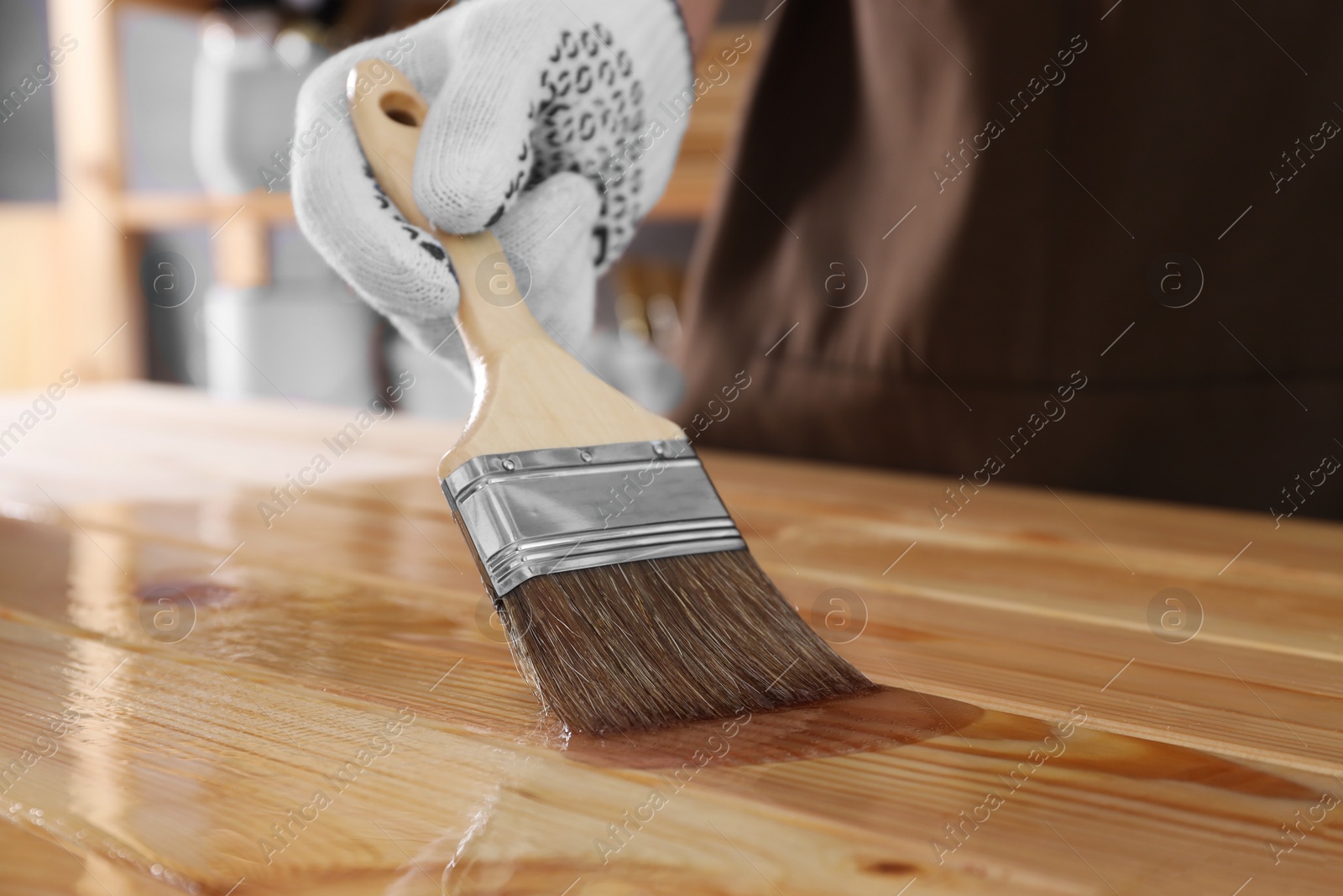 Photo of Man varnishing wooden surface with brush indoors, closeup