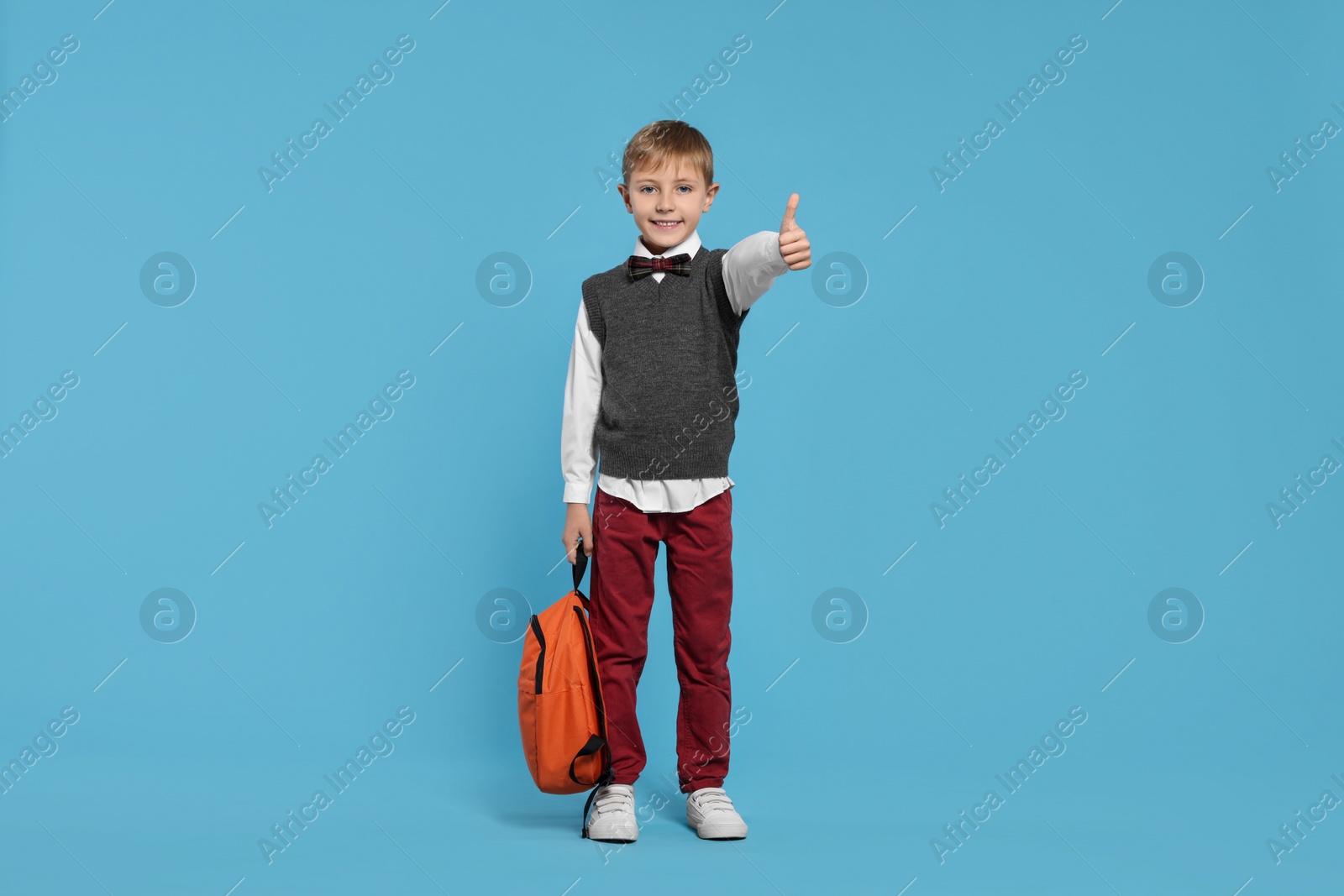 Photo of Happy schoolboy with backpack showing thumb up gesture on light blue background