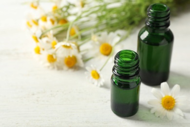 Photo of Chamomile flowers and cosmetic bottles of essential oil on wooden table, closeup. Space for text