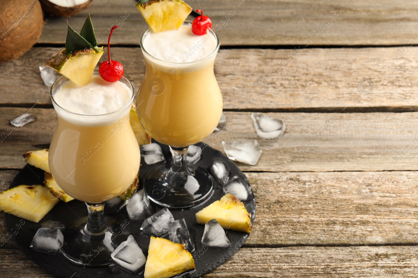 Photo of Tasty Pina Colada cocktails and ingredients on wooden table, space for text