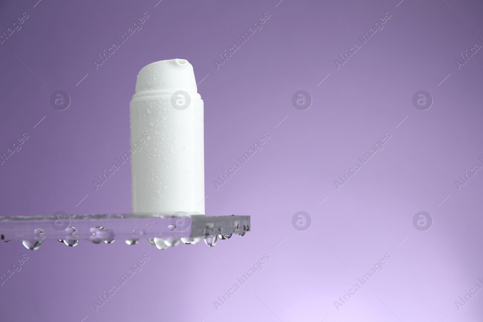 Photo of Moisturizing cream in bottle on glass with water drops against violet background. Space for text