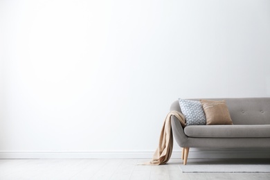 Photo of Grey sofa with pillows near white wall in stylish living room interior. Space for text