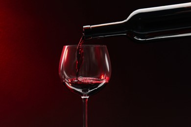 Photo of Pouring red wine from bottle into glass on dark background, space for text