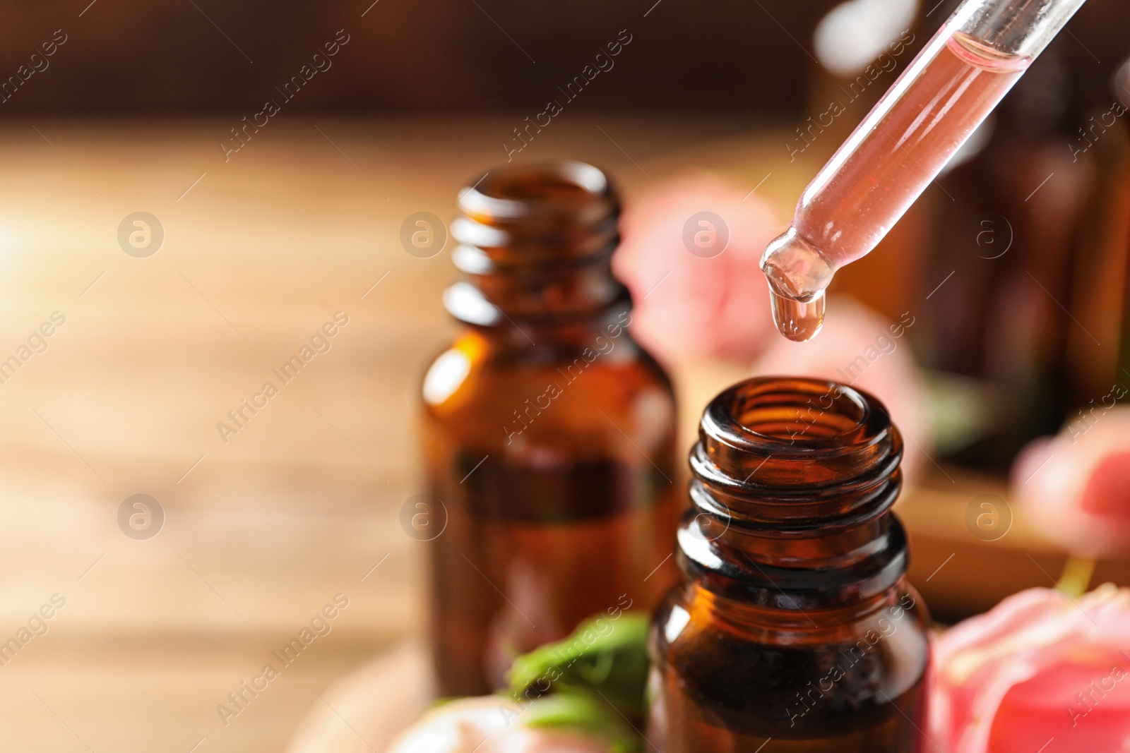 Photo of Dripping rose essential oil into bottle against blurred background, space for text