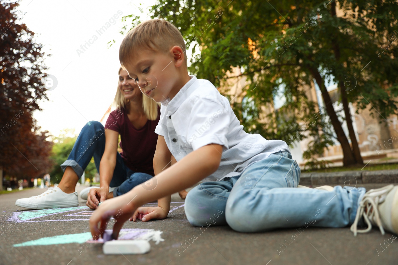 Photo of Nanny with cute little boy drawing house with chalks on asphalt