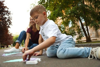 Nanny with cute little boy drawing house with chalks on asphalt