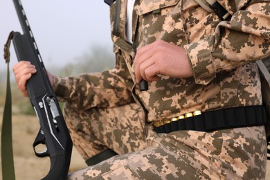 Photo of Man wearing camouflage with hunting rifle and cartridge outdoors, closeup