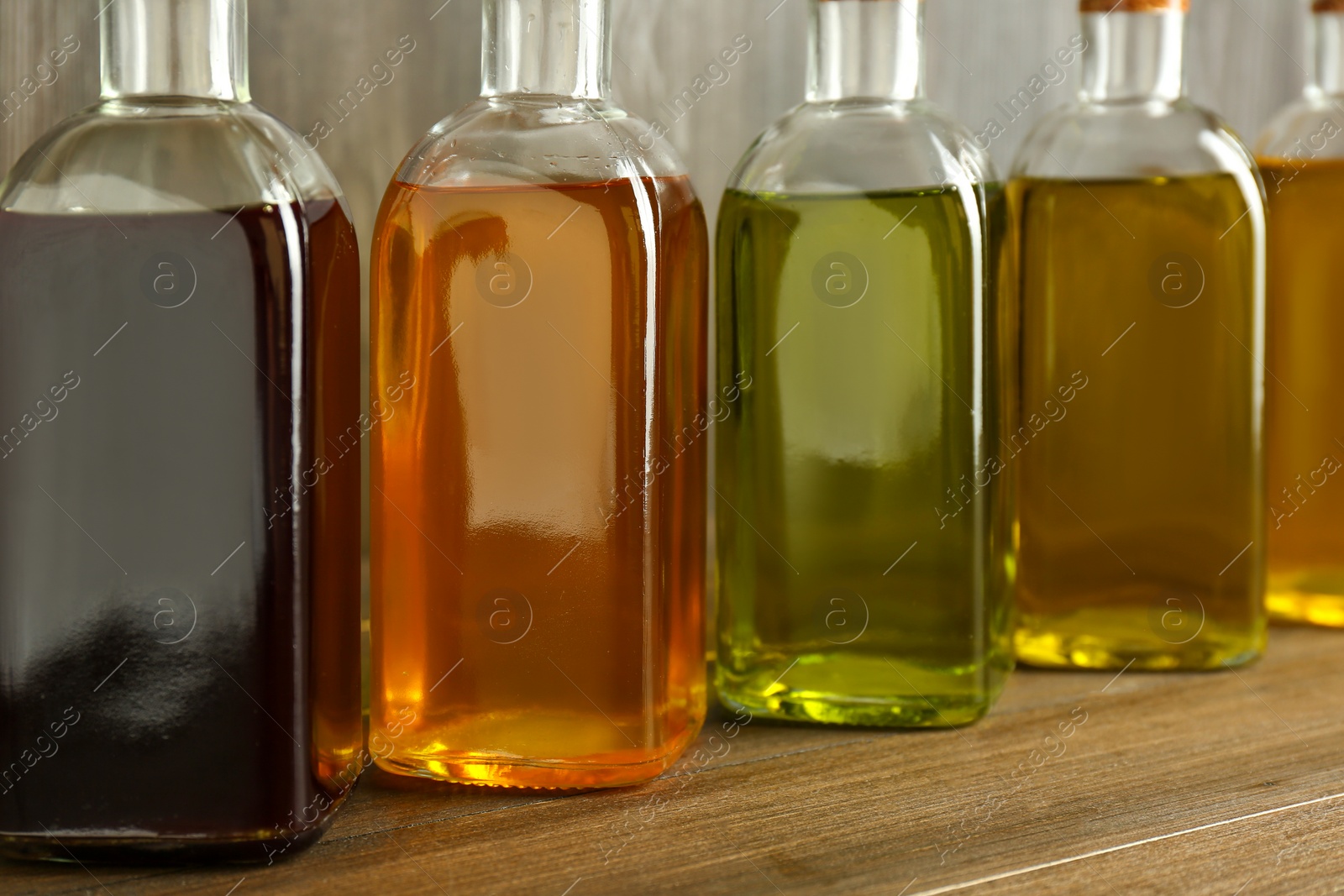 Photo of Vegetable fats. Different oils in glass bottles on wooden table, closeup