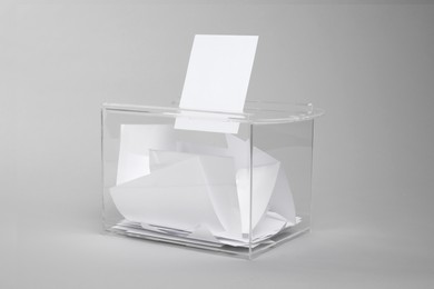 Photo of Ballot box with votes on light grey background. Election time