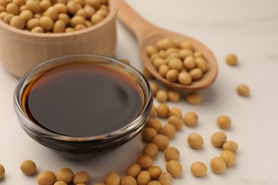 Soy sauce in bowl and soybeans on white table, closeup