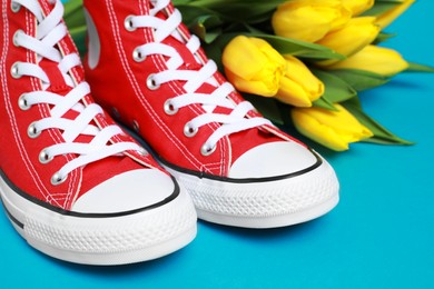 Photo of Pair of new stylish red sneakers and beautiful tulips on light blue background, closeup