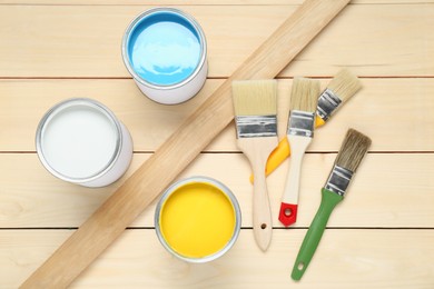 Cans of different paints and brushes on wooden table, flat lay