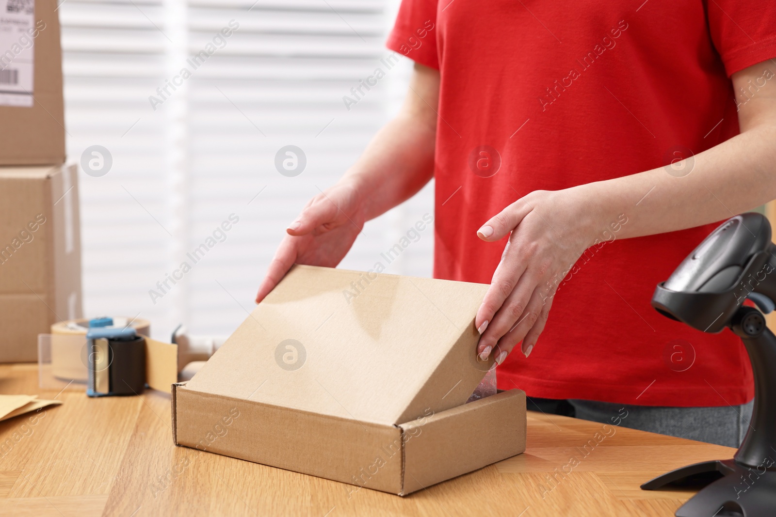 Photo of Post office worker packing parcel at wooden table indoors, closeup