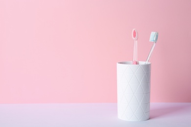 Photo of Cup with toothbrushes on table against color background. Dental care