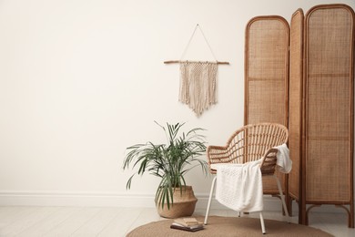 Photo of Stylish wooden chair, folding screen and beautiful houseplant near white wall in room. Space for text