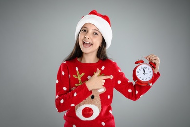 Girl in Santa hat with alarm clock on grey background. Christmas countdown