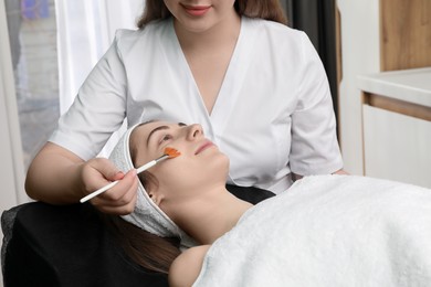 Photo of Cosmetologist with brush applying cosmetic product to client`s face in clinic, closeup