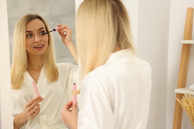 Photo of Beautiful woman applying mascara near mirror in bathroom