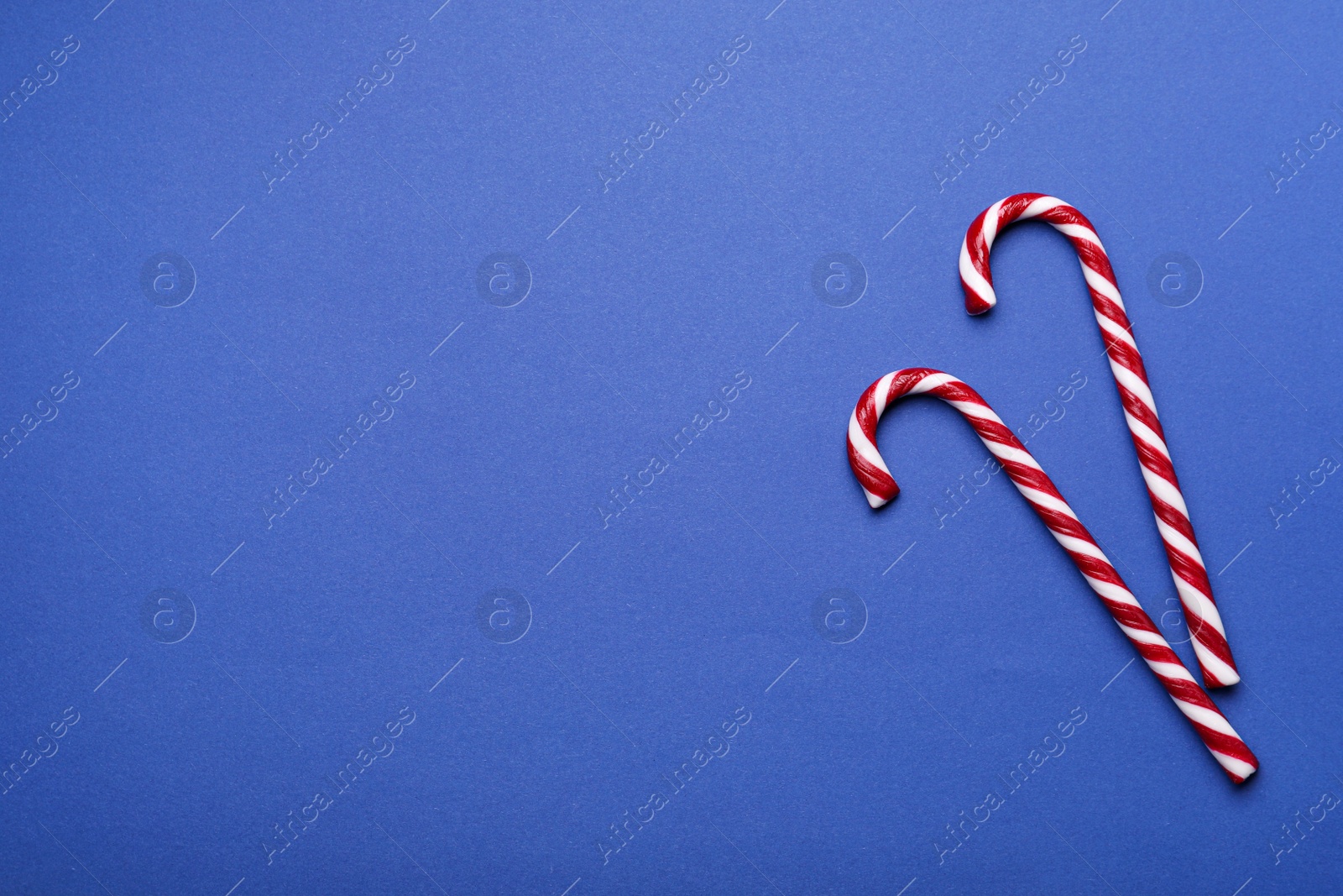 Photo of Two sweet Christmas candy canes on blue background, flat lay. Space for text