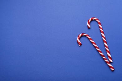 Photo of Two sweet Christmas candy canes on blue background, flat lay. Space for text