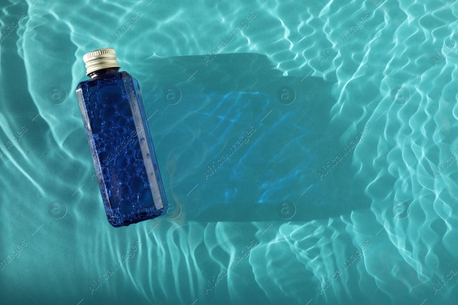 Photo of Bottle of cosmetic product in water on turquoise background, top view. Space for text