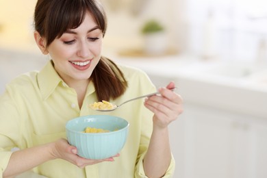 Smiling woman eating tasty cornflakes at breakfast indoors. Space for text