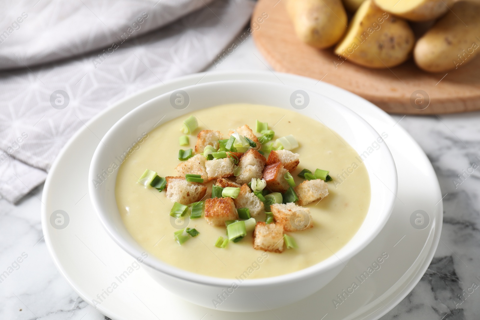 Photo of Tasty potato soup with croutons and green onion in bowl on white marble table