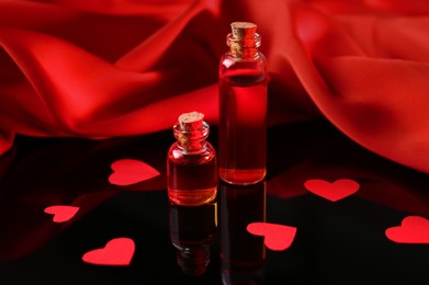 Photo of Bottles of love potion, paper hearts and red fabric on mirror surface