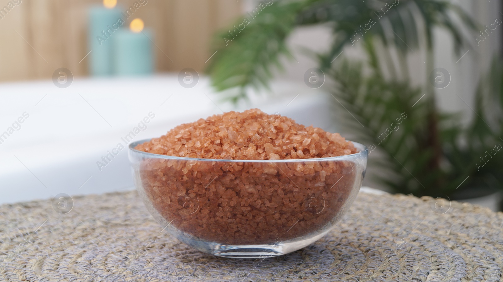 Photo of Glass bowl of bath salt on wicker mat in bathroom