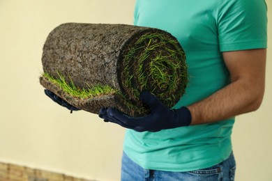 Photo of Young man holding rolled grass sod at backyard, closeup