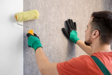 Man hanging stylish gray wallpaper in room