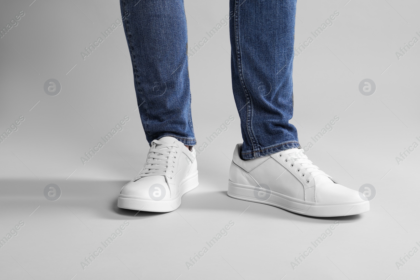 Photo of Man wearing stylish white sneakers on grey background, closeup